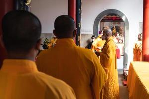 Bandung City, Indonesia, 2022 - The monks in orange rob standing in order while praying to the god at the altar inside the Buddha temple photo