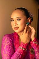 Asian woman in a pink dress trying to wear a green earring in her ears photo