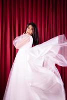 Beautiful Asian woman posing in a flying wedding dress in front of the red curtain photo