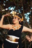 A beautiful Javanese woman poses with her hand in a black costume while wearing a golden crown and golden necklace photo