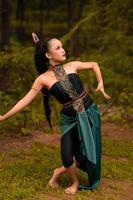 Indonesian woman with long black hair wearing a green costume with makeup in front of the forest photo