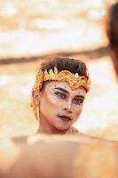 An Asian man faces in makeup with a golden crown on her head looks angry while posing photo