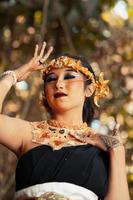 A beautiful Javanese woman poses with her hand in a black costume while wearing a golden crown and golden necklace photo