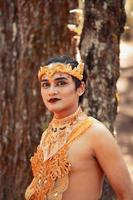 Balinese man standing in the forest while wearing a gold crown and golden necklace photo