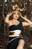 Balinese woman sitting beautifully on the rock in a black dance costume with makeup on her face and a gold crown on her head photo