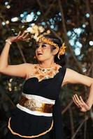 A beautiful Javanese woman poses with her hand in a black costume while wearing a golden crown and golden necklace photo