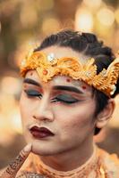 Asian man with a thinking expression while wearing a gold crown and gold necklace on her body photo