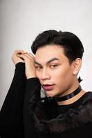 Pretty Asian man putting his hand and head on the chair while posing in a black dress photo