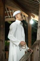 A Muslim man standing on the balcony of a wooden house in the village photo