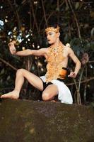 Asian man sitting down on his knee while wearing a gold costume and golden crown on the top of the big rock photo