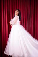 Beautiful Asian woman standing with a happy face in a white wedding dress in front red curtain photo