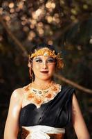 Javanese woman with golden crown and black costume chilling inside the forest while wearing makeup photo