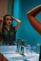 Indonesian woman staring the mirror of herself wearing a black dress with wet body and wet hair photo