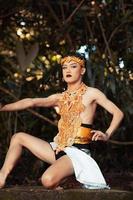 Asian man sitting down on his knee while wearing a gold costume and golden crown on the top of the big rock photo