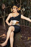 Balinese woman sitting beautifully on the rock in a black dance costume with makeup on her face and a gold crown on her head photo