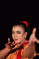 A Balinese woman poses with both her hands in a traditional orange dress and red scarf on her body photo