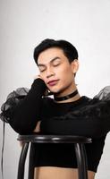 beautiful Asian man posing with the chair while wearing a black costume and makeup photo