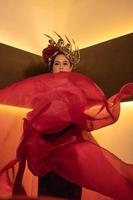 A glamor woman poses with a flying red dress on her body while wearing a gold crown photo