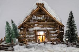 casa de madera en miniatura y árboles de navidad en la nieve. foto