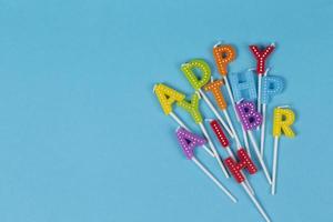 Colorful candles in letters with  Happy Birthday  lettering isolated on blue background.Happy birthday letters mixed up. photo