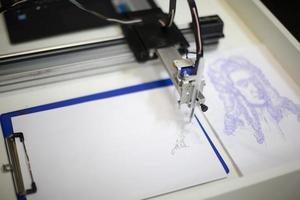 bielorrusia, ciudad de gomel, 11 de enero de 2022. festival de robots. la mano del robot hace un dibujo. mano robot con lápiz dibuja dibujos gráficos simples en papel blanco foto