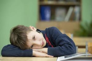 Tired little boy put his head on the school desk. Child at school. photo