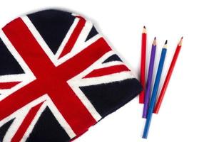Winter knitted hat with a pattern of the UK flag and colored pencils on a white background. photo