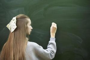 una adolescente en edad de escuela secundaria escribe con tiza en una pizarra. foto