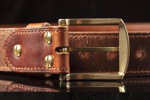 Part of a leather brown belt with a metal buckle on a black background. photo