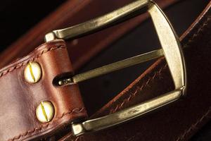 parte de un cinturón marrón de cuero con una hebilla de metal sobre un fondo negro. foto