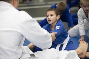 Belarus, city of Gomil, December 15, 2021. Judo school for children. The trainer stretches the child in kimano. photo