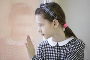 Sad child looks out the window, feels lonely. Thoughtful girl is unhappy with the problem. Difficult adolescence concept. photo