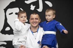 Belarus, city of Gomil, December 15, 2021. Judo school for children. The judo coach holds little students in kimano in her arms. photo