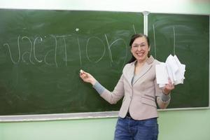 Happy teacher writes the word vacation on the blackboard. photo