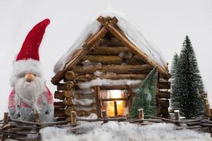 A fabulous Christmas gnome stands next to a miniature wooden house. photo