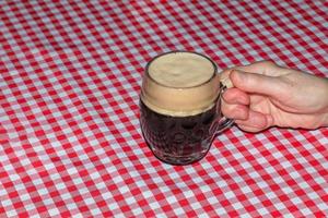 A mug of beer on a table covered with a red checkered tablecloth. photo