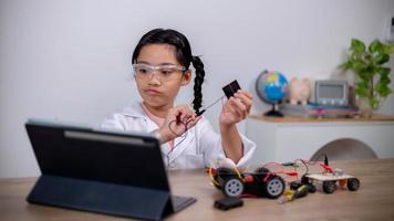 los estudiantes asiáticos aprenden en casa codificando automóviles robot y cables de placas electrónicas en tallo, vapor, ingeniería matemática, ciencia, tecnología, código informático en robótica para conceptos infantiles. foto