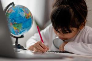 Asian schoolgirl doing her homework with laptop at home. Children use gadgets to study. Education and distance learning for kids. Homeschooling during quarantine. Stay at home photo