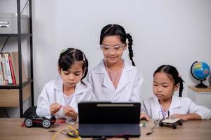 los estudiantes asiáticos aprenden en casa codificando automóviles robot y cables de placas electrónicas en tallo, vapor, ingeniería matemática, ciencia, tecnología, código informático en robótica para conceptos infantiles. foto