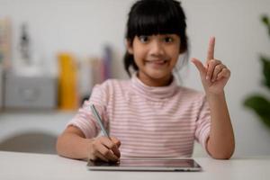 Asian little cute girl touching the digital tablet screen on the table photo