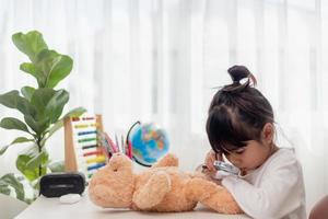 niño jugando con oso de peluche. niña asiática abrazando su juguete favorito. niño y animal de peluche en casa. foto