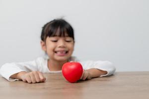 retrato de una niña asiática con un cartel de corazón rojo en el fondo blanco foto