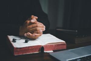 Christian online technology concept. Hands praying of christian with digital computer laptop, Online live church for sunday service. Asian catholic man are reading Holy bible book and online study. photo