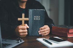 Christian online technology concept. Hands praying of christian with digital computer laptop, Online live church for sunday service. Asian catholic man are reading Holy bible book and online study. photo