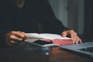 concepto de tecnología cristiana en línea. manos rezando de cristiano con computadora portátil digital, iglesia en vivo en línea para el servicio dominical. el hombre católico asiático está leyendo el libro sagrado de la biblia y estudiando en línea. foto