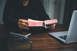 concepto de tecnología cristiana en línea. manos rezando de cristiano con computadora portátil digital, iglesia en vivo en línea para el servicio dominical. el hombre católico asiático está leyendo el libro sagrado de la biblia y estudiando en línea. foto