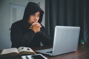 Christian online technology concept. Hands praying of christian with digital computer laptop, Online live church for sunday service. Asian catholic man are reading Holy bible book and online study. photo