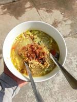 a bowl of Indonesian food called soto which is made from vermicelli noodles, pieces of chicken, and some vegetables photo