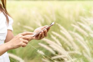 Young asian woman using smartphone in the flower field while traveling in summer photo