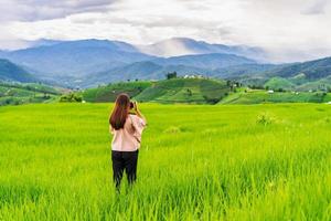 Young woman traveler on vacation taking a picture at beautiful green rice terraces field in Pa Pong Pieng, Chiangmai Thailand photo